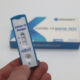 Eine Hand hält einen positiven Covid-Schnelltest. Im Hintergrund liegt die Packung des Tests.